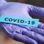 Hand med plasthandske som håller en lapp med texten covid-19